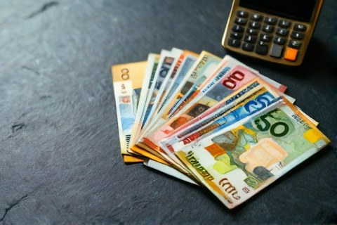 Banknotes of several world currencies fanned out next to a bank card and a calculator